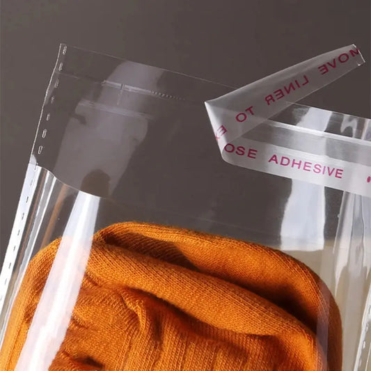 Transparent self-sealing storage bag with orange garment inside showing adhesive closure - DTF transfer storage bag UK
